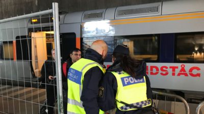 Två poliser i reflexväst står framför ett tåg och kollar en mans id.