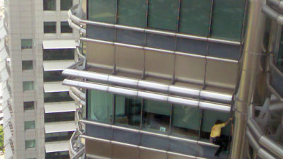 En man i gul tröja klättrar på en hög byggnad.