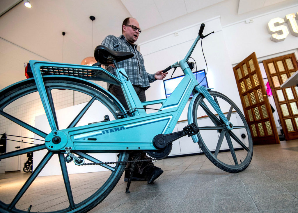 En man står bakom en blå cykel i plast.