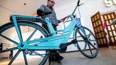 En man står bakom en blå cykel i plast.