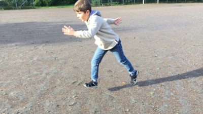 Ayham har blå byxor och ljus jacka. Han är mitt i ett steg och springer över en grusplan.