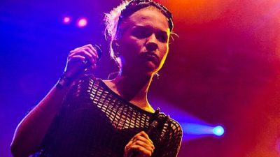 Tove Stryke står på scen med färgat ljus bakom sig och en mick i handen.