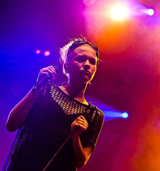 Tove Stryke står på scen med färgat ljus bakom sig och en mick i handen.