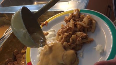 Mat läggs upp på en tallrik i en skolmatsal.