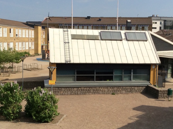 Bild på skolgård med buskar, hus och grus.