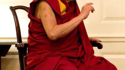 Dalai Lama sitter på en stol i en röd kläsel