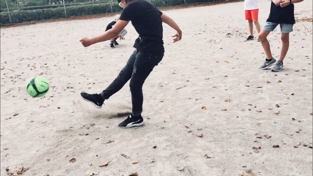 Fyra barn spelar fotboll på grusplan.