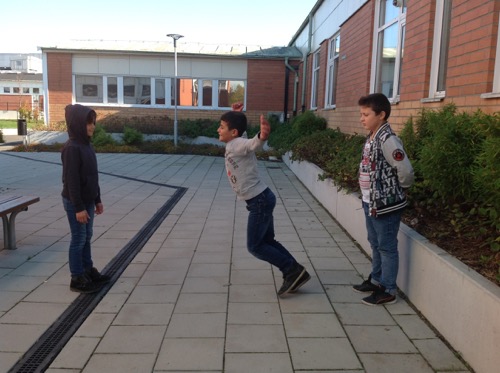 Tre barn leker intill skolbyggnad.