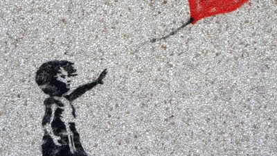 Ett barn som sträcker sig efter en hjärtformad röd ballong är målad på en grå mur.