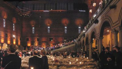 En bild på en stor sal med en stor trappa längst bort. I hela hallen är det fullt med långbord med fina dukar och porslin.