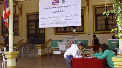 Bilden visar en vallokal. En person böjer sig fram över ett bord för att fylla i sina uppgifter för att få rösta.