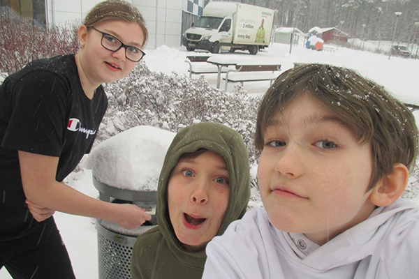 Foto på tre elever framför en soptunna på en snöig skolgård.