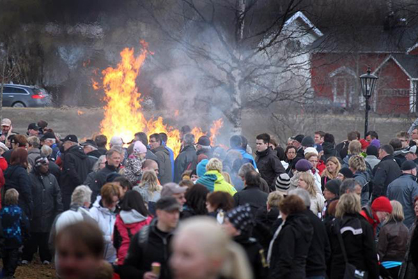 Foto på folksamling som står runt en stor brasa.