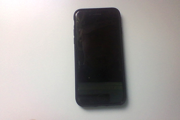 Foto på en svart mobiltelefon som ligger på ett vitt bord.