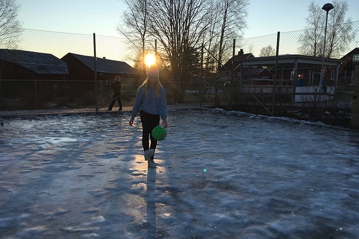 Tjej som trixar med en fotboll på en fotbollsplan som är täckt av is.